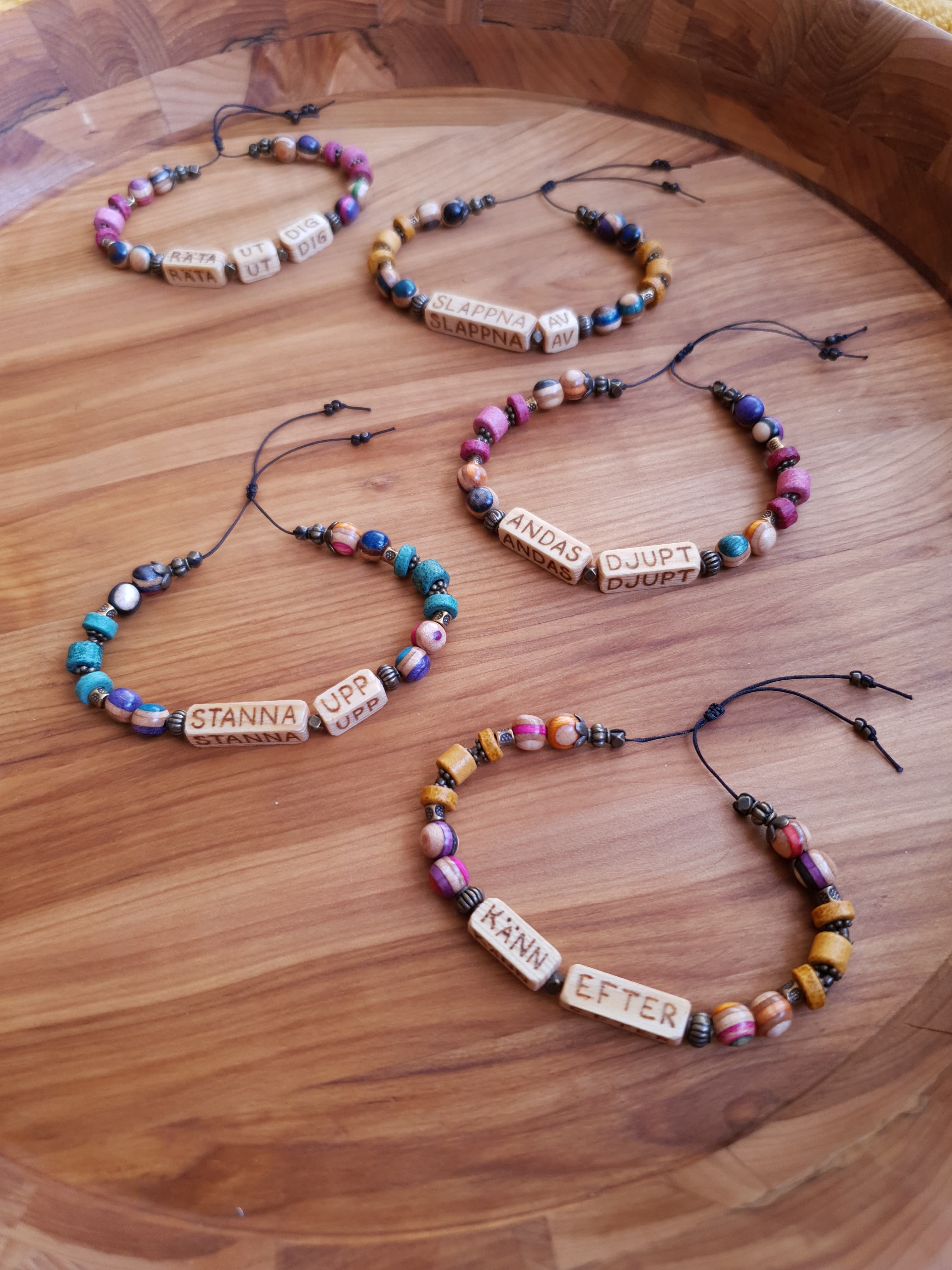 Five hippie-looking bracelets with different expressions on them. The expressions are 'räta ut dig', 'slappna av', 'andas djupt', 'stanna upp' and 'känn efter'.
